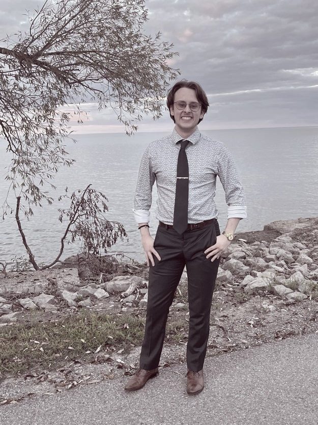 Daniel Woytowich standing by the water in a white shirt and tie